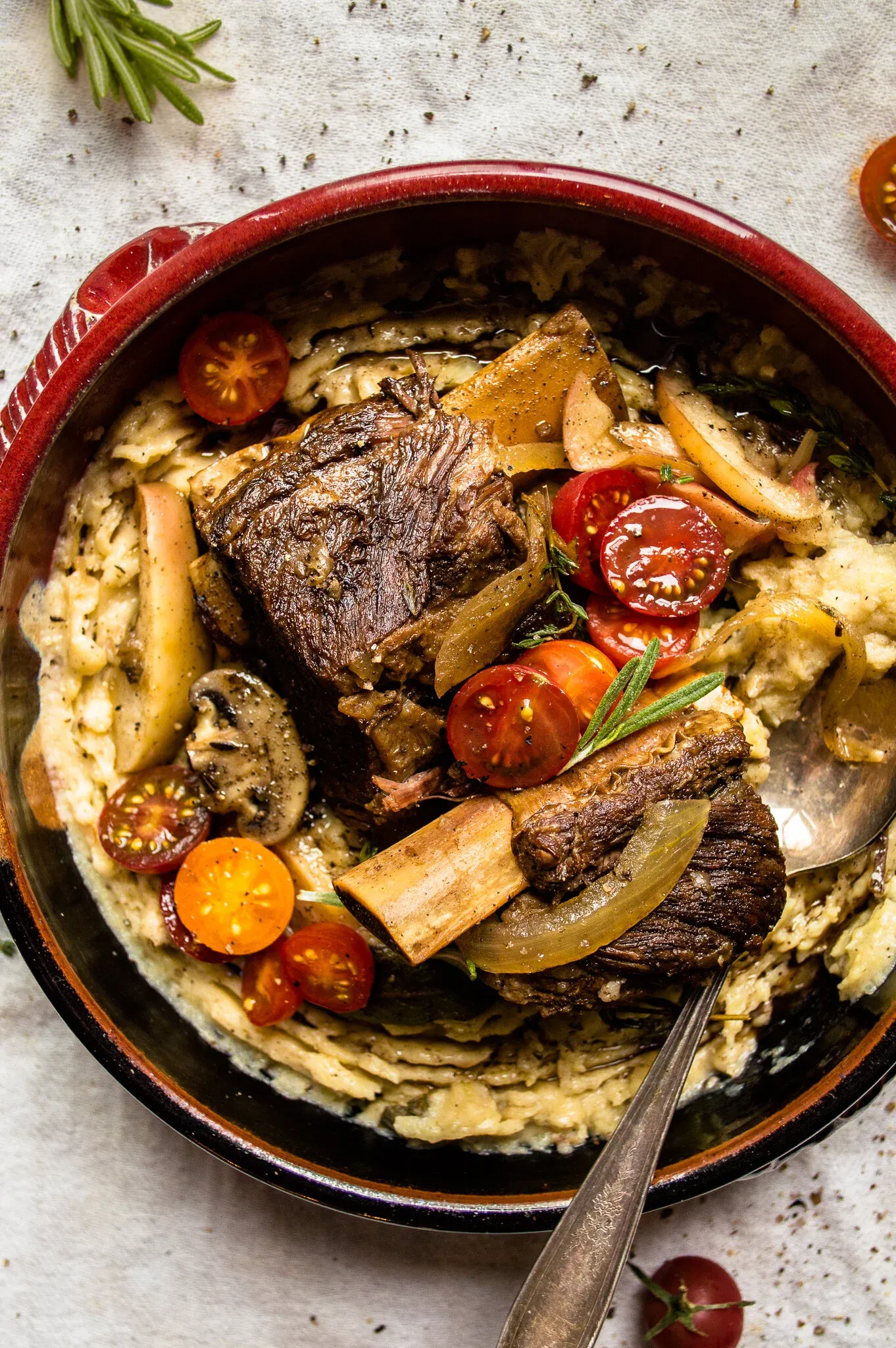 Slow cooker hard cider braised short ribs with brown butter mashed potatoes served in a dark ceramic bowl with red rim