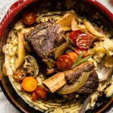 Slow cooker hard cider braised short ribs with brown butter mashed potatoes served in a dark ceramic bowl with red rim