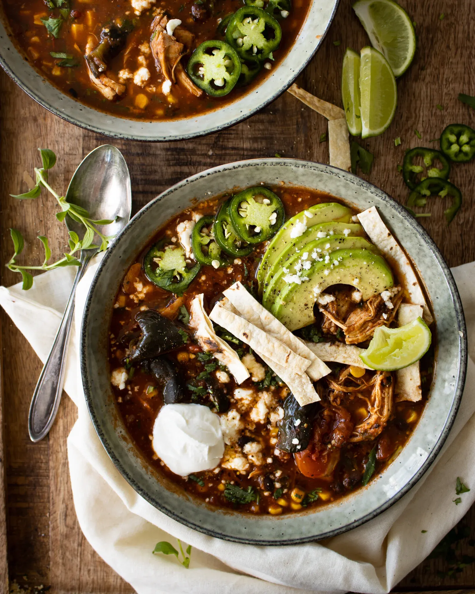 Two matte gray-rimmed ceramic bowls of Chicken Tortilla Soup arranged overhead on a dark wood table