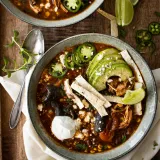 Two matte gray-rimmed ceramic bowls of Chicken Tortilla Soup arranged overhead on a dark wood table