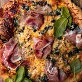 Spinach and Artichoke Pizza in a very close overhead crop on a wooden board