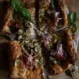 Artichoke and Mushroom Tart sliced into rectangular pieces on a round wooden board over parchment paper
