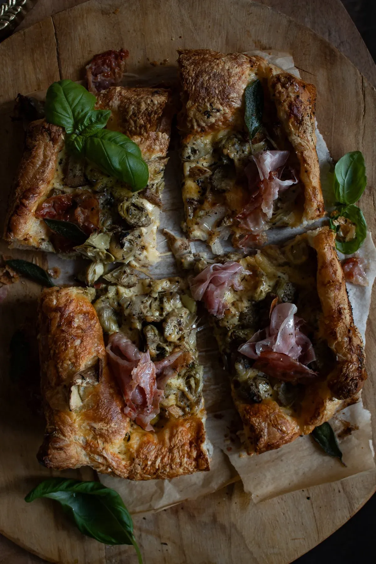 Artichoke and Mushroom Tart sliced into rectangular pieces on a round wooden board over parchment paper