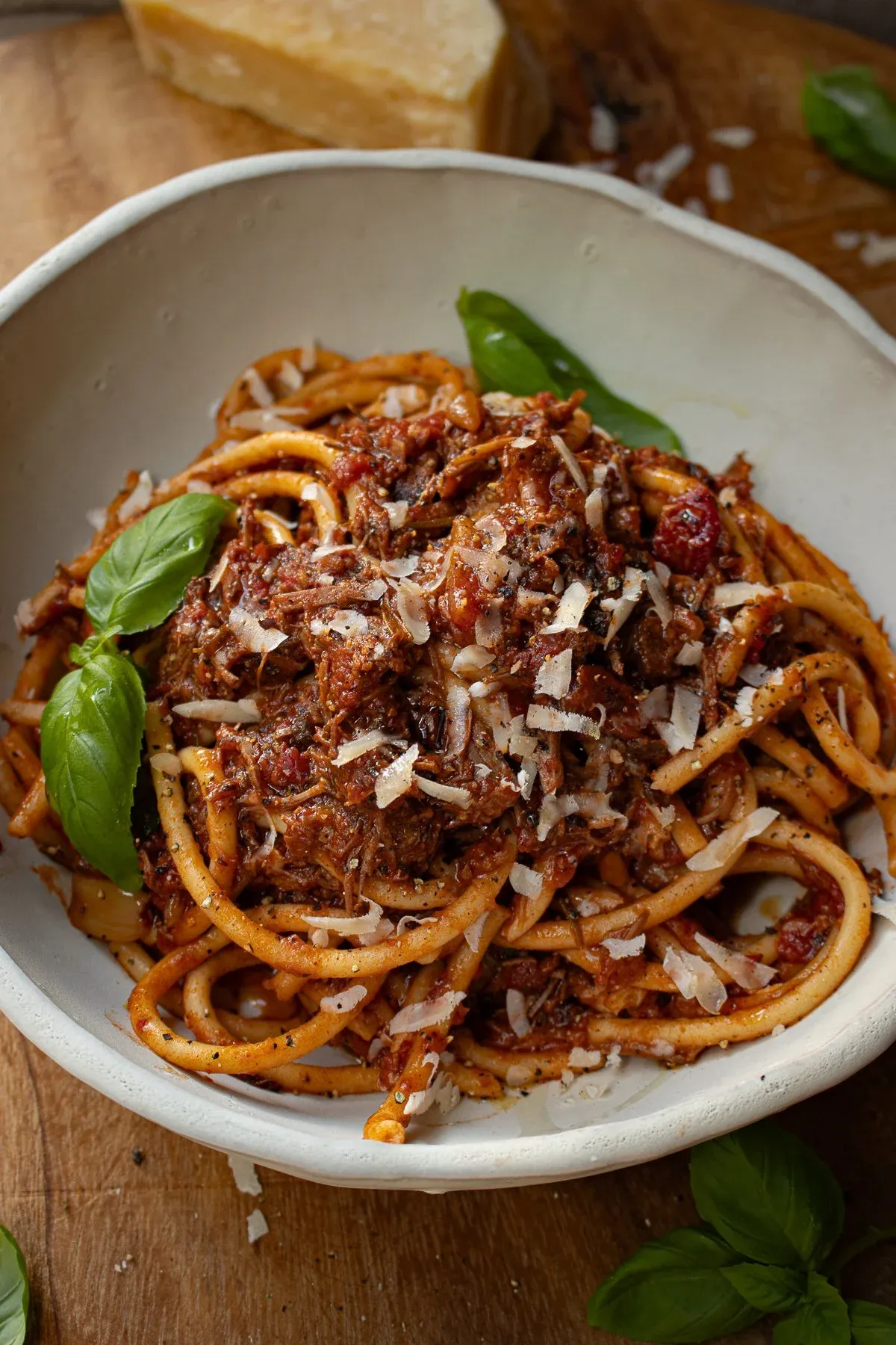 White rustic bowl of Dominican Style Goat Ragù served over thick bucatini pasta coated in a deep-red tomato-braised goat sauce