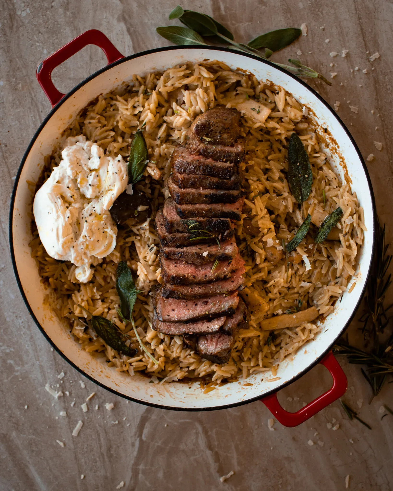 Overhead shot of Brown Butter Orzo with Steak in a white enamel wide pan with red handles; toasted amber orzo fills the pan