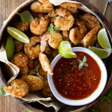 Overhead shot of a round wooden bowl filled with golden-brown Coconut Crusted Oven Fried Shrimp tails-on