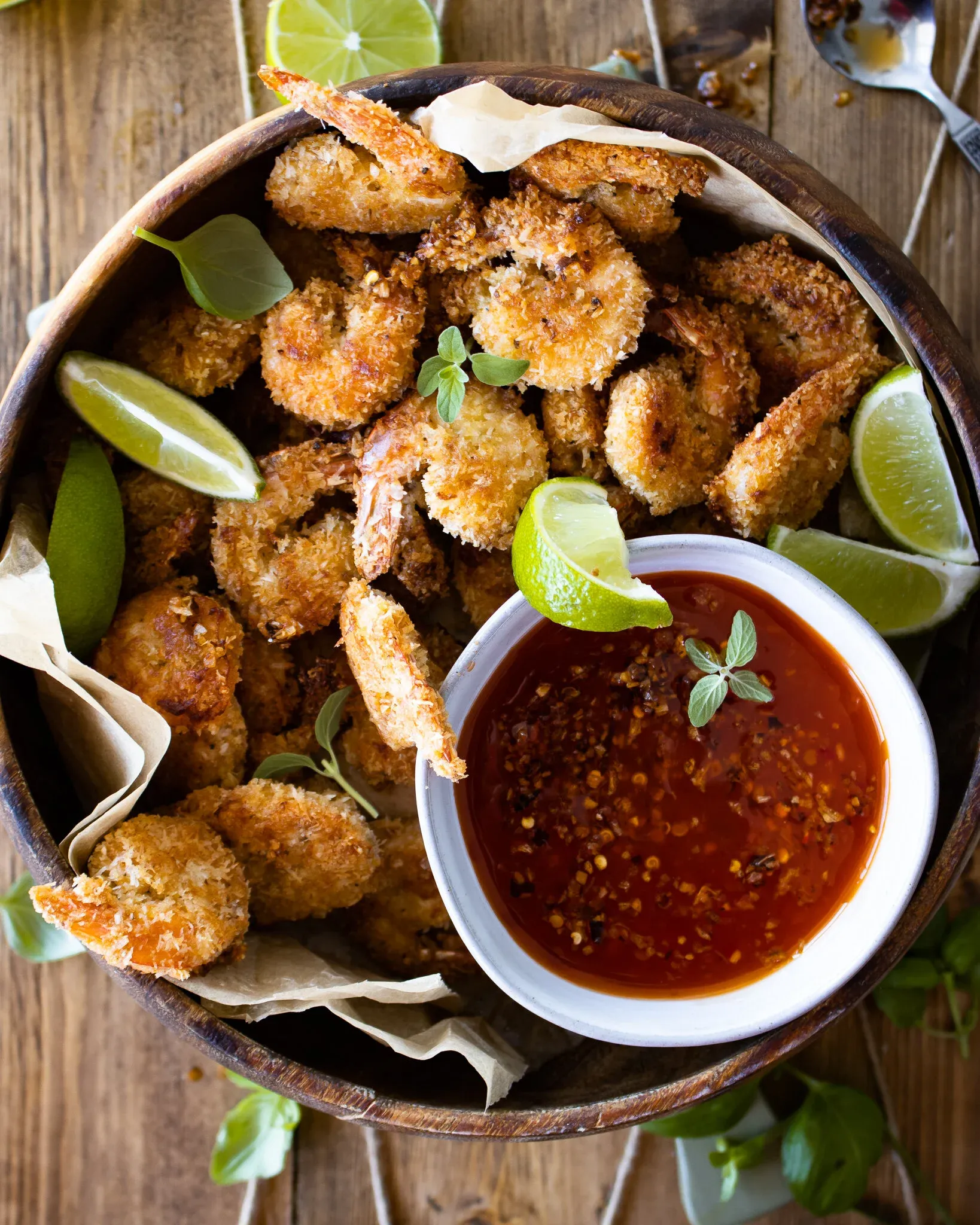 Overhead shot of a round wooden bowl filled with golden-brown Coconut Crusted Oven Fried Shrimp tails-on