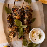 Three Grilled Chicken Skewers with Garlicky Whipped Ricotta on an oval white ceramic platter lined with parchment