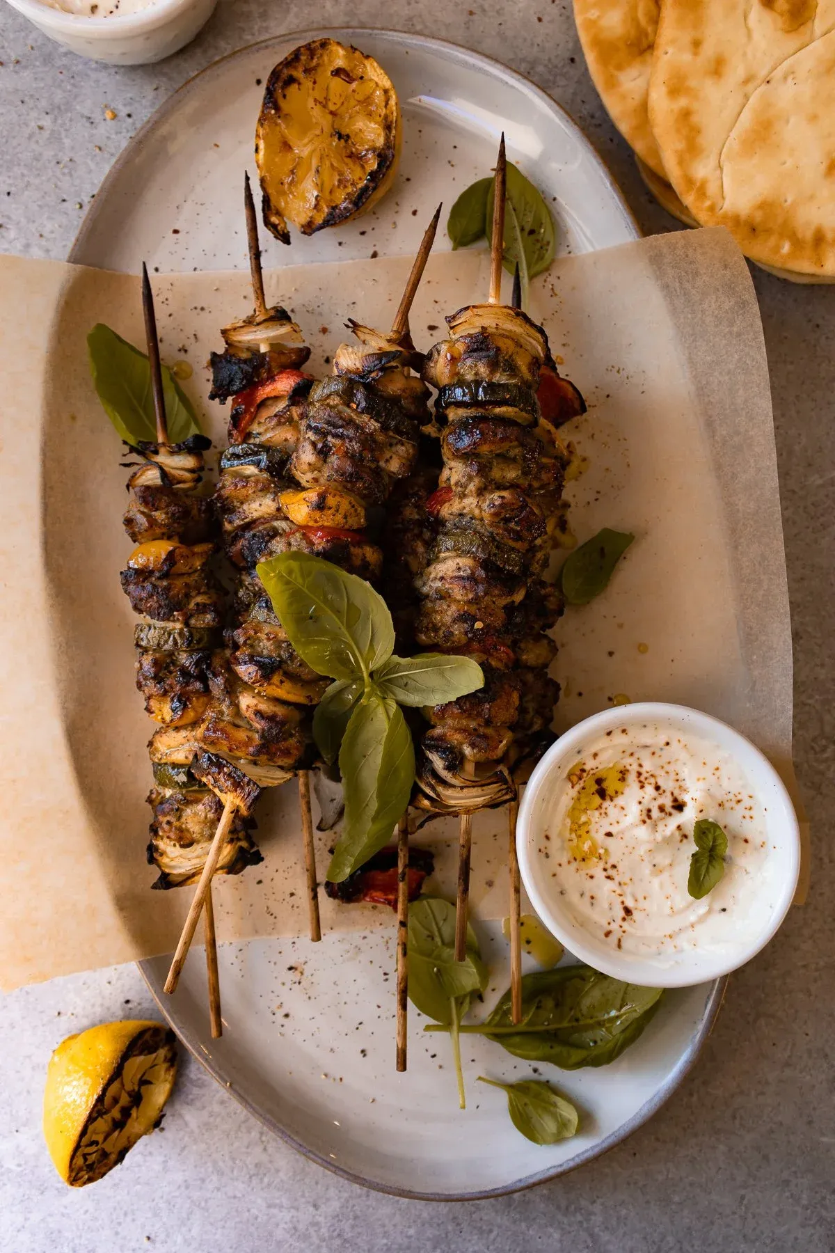 Three Grilled Chicken Skewers with Garlicky Whipped Ricotta on an oval white ceramic platter lined with parchment
